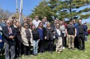 Gathering of about two dozen people posing for a photo outdoors in front of a soldier's memorial