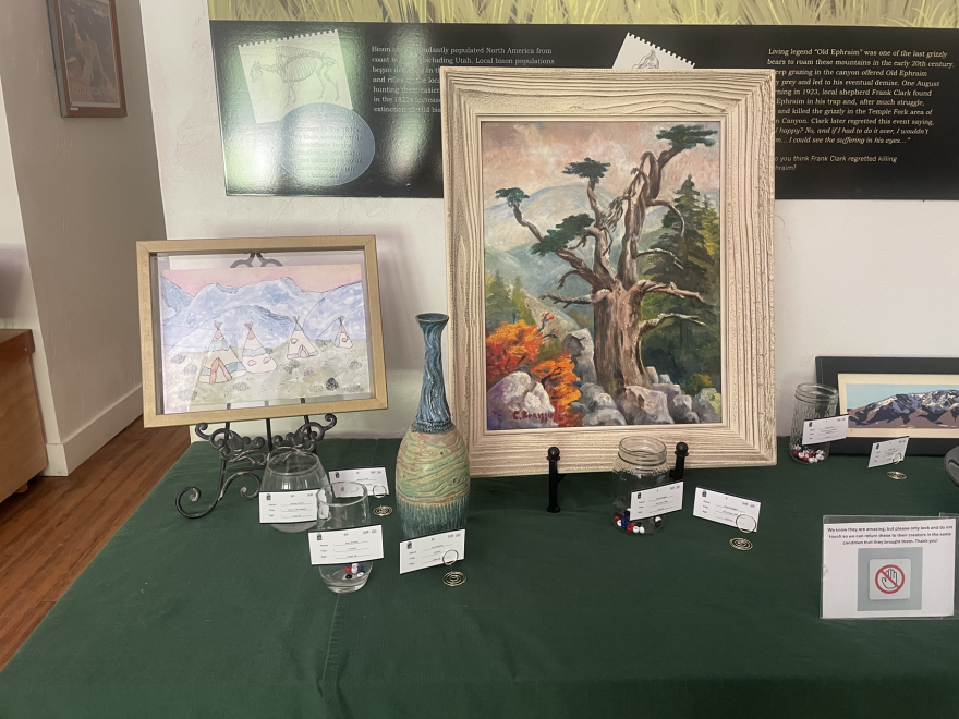 A painting of a tree, a drawing of Native American tent dwellings, and a narrow-necked vase.
