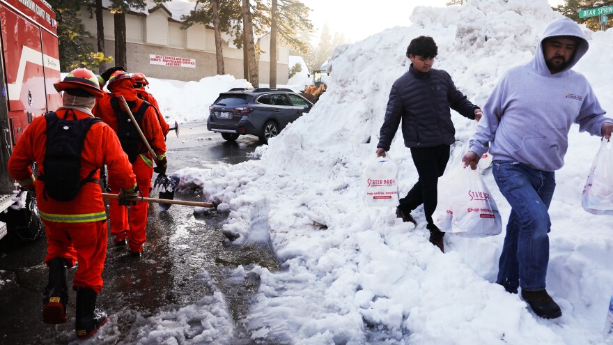 A crew of inmate firefighters walk back to their vehicle after shoveling and clearing snow, while people carry bags of food on Friday. A series of winter storms in the San Bernardino Mountains in Southern California left residents stranded due to the snowfall.