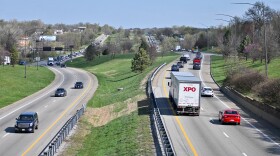 A highway divided by a grassy median shows traffic moving both directions on a sunny day.