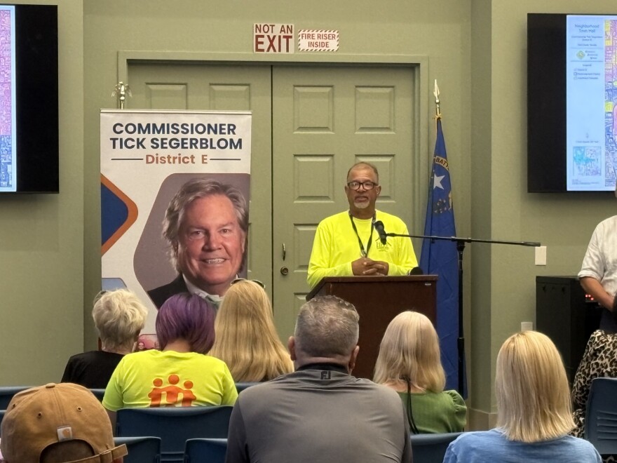 Louis Lacey of HELP of Southern Nevada stands behind a podium and addresses a crowd of seated locals.