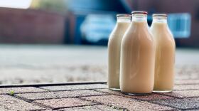 Three bottles of milk sitting on the ground.