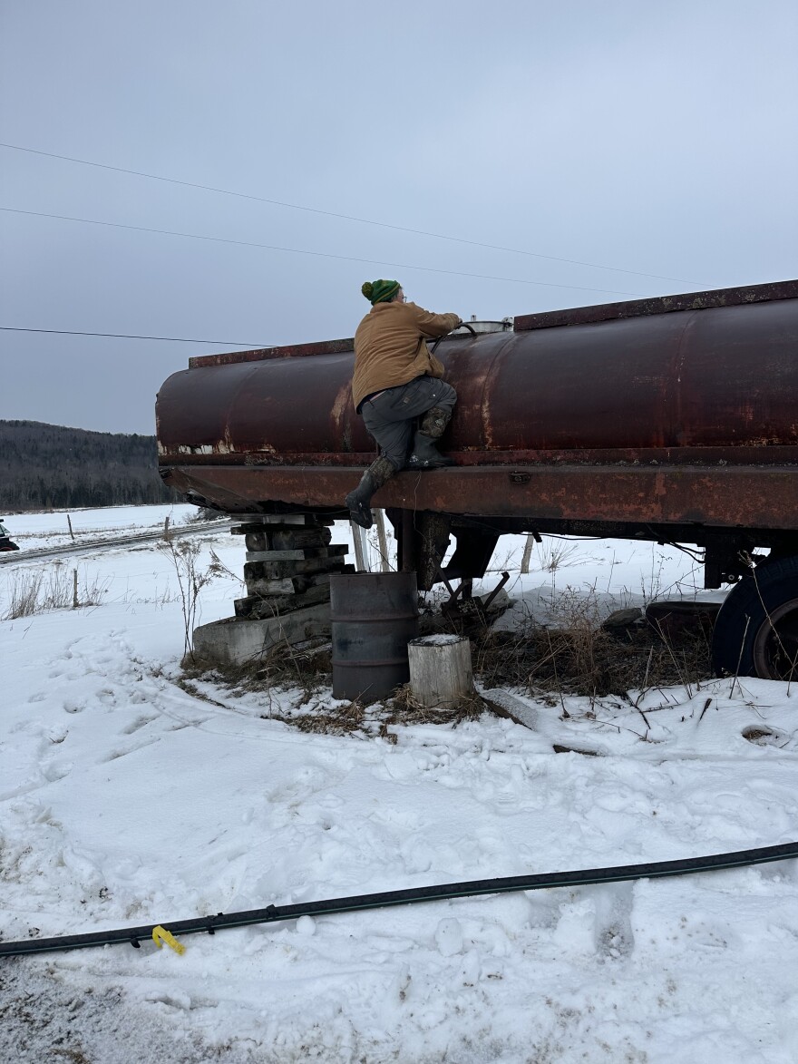 Man standing on a giant maple sap tank with snow in foreground