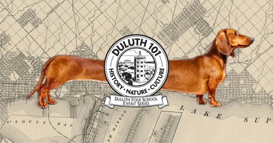 A dachshund dog, stretched out over an old map of a town; a black and white emblem in front with "Duluth 101" written on it