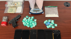 money, drugs, cell phones and a gun seized by police in a drug bust are laid out on an office desk.