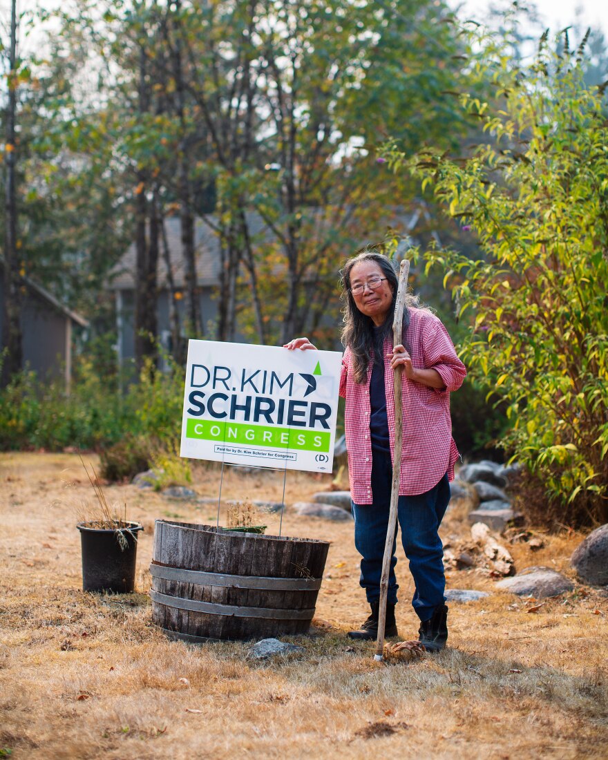 A woman poses next to a political sign with trees in the background. 