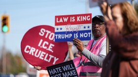 Protesters hold signs during the arrival of federal law enforcement, Wednesday, Nov. 19, 2025, in Charlotte, N.C.