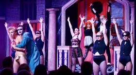 Nine cast members of the Rocky Horror show dance in theatrical clothing on stage during a live performance. 