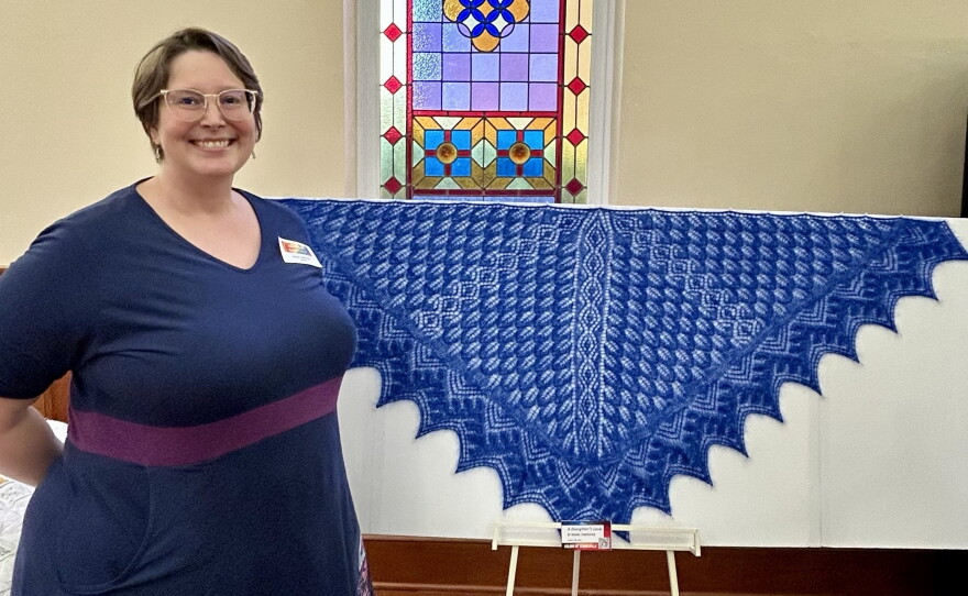 Rachel Carpenter stands next to the lace shawl she made for her mother’s 70th birthday and remembrance.