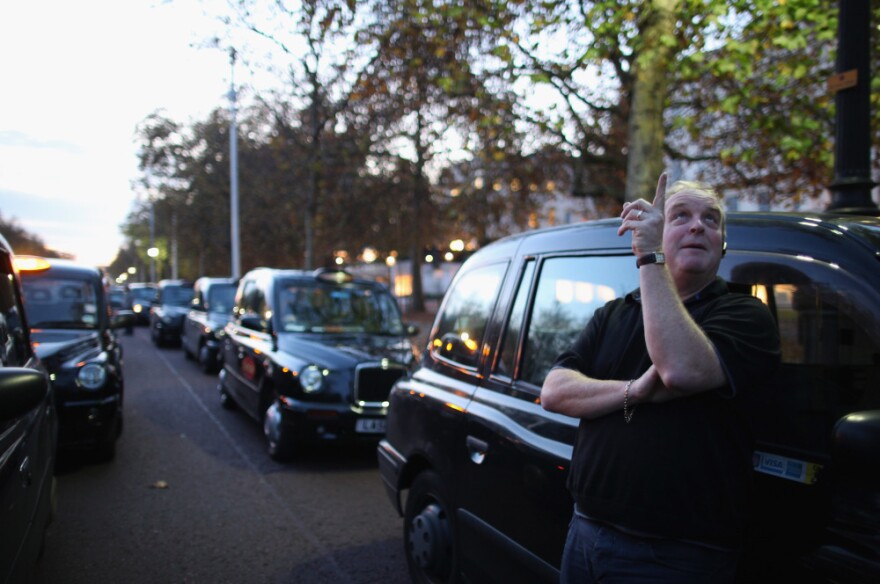 A taxi driver stands outside his cab in London, England. 