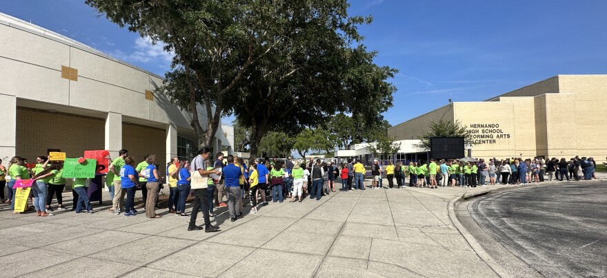  Large group of people gathered outside in a formed line standing in front of a school building. 