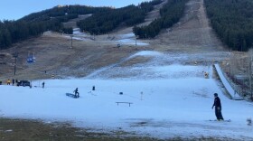 Skiers navigate on a small patch of snow on an otherwise green field.
