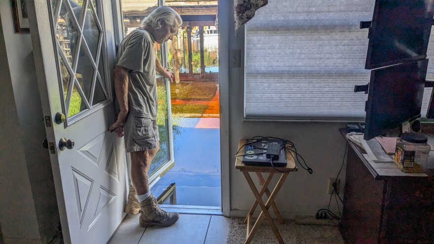 A man opens his back door to show how high floodwaters have risen.
