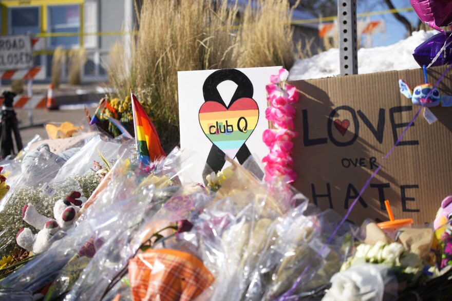 A close-up of flowers and signs that say "CLUB Q" and "LOVE OVER HATE" 