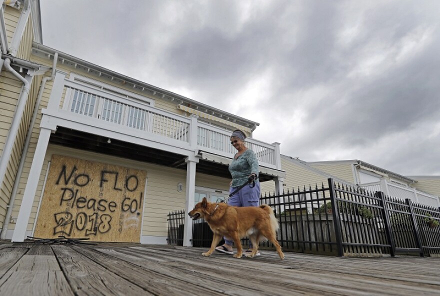 Barbara Timberlake walks with her dog Danny past a boarded up store on the river front in downtown Wilmington, N.C., as Hurricane Florence threatens the coast Thursday, Sept. 13, 2018.