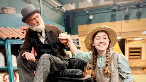 An actor on a horse buggy holding the hand of a girl wearing a straw hat.