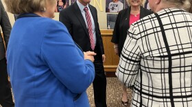 John Craft wears a black suit and red striped tie while talking in a group of people in the boardroom of Northside ISD.