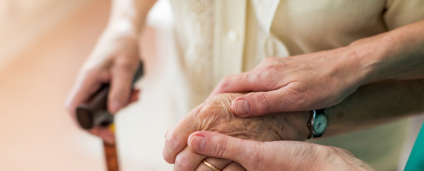 Woman holds hand of an elderly woman holding a cane.