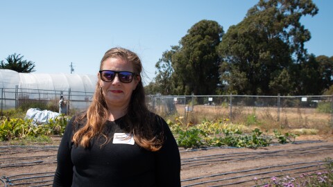 A woman stands in front of a small plot of land covered in drip irrigation tape with flowers in the foreground. 