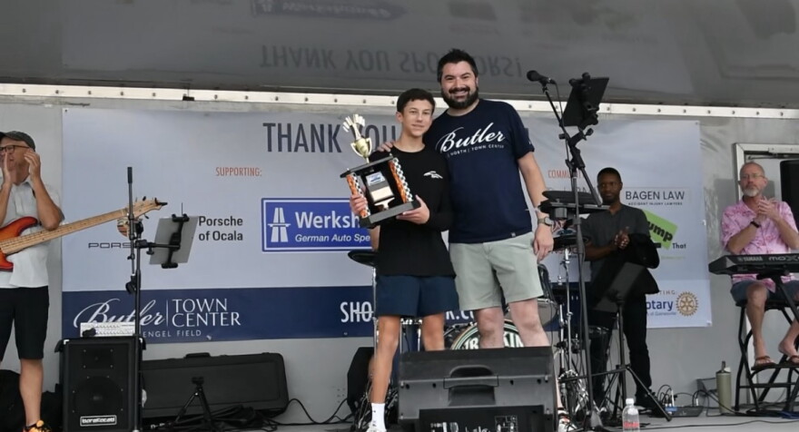 Oscar Astrom, left, accepts the People’s Choice Award on behalf of his father at the Sixth Annual International Motorcycle and Car Meet in Gainesville, Saturday, Oct. 17, 2026. (Courtesy of Harris Marcus)