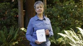 Karen McKnight stands in her backyard on Saturday, June 19, 2021, in Sammamish, Wash., holding two books written by her brother Ross Bagne of Cheyenne, Wyo.