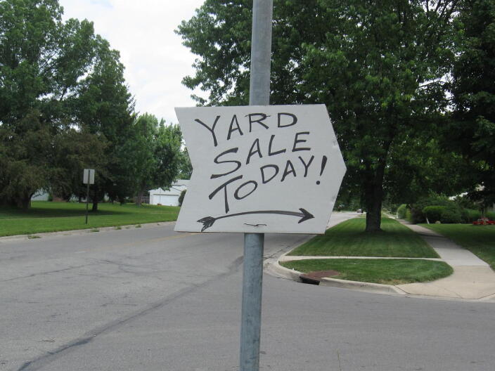 A white yard sale sign points in the direction of a sale.