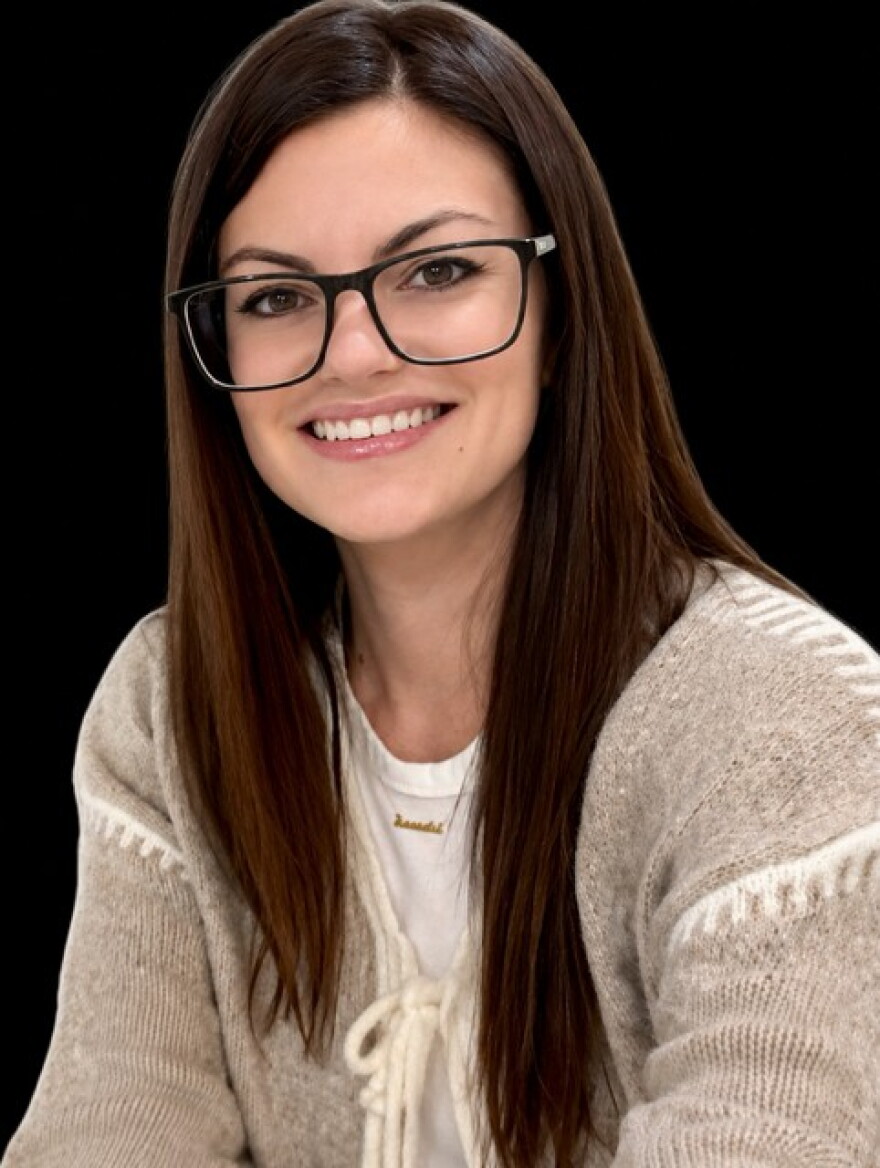 A woman with glasses smiles at the camera