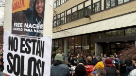 People gather outside a building. In the foreground is a sign that reads  "Free Nacho! and No estan solos!"