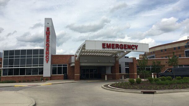 A dark van pull into the circle in front f a building marked with the word, "Emergency" in red at the entrance.