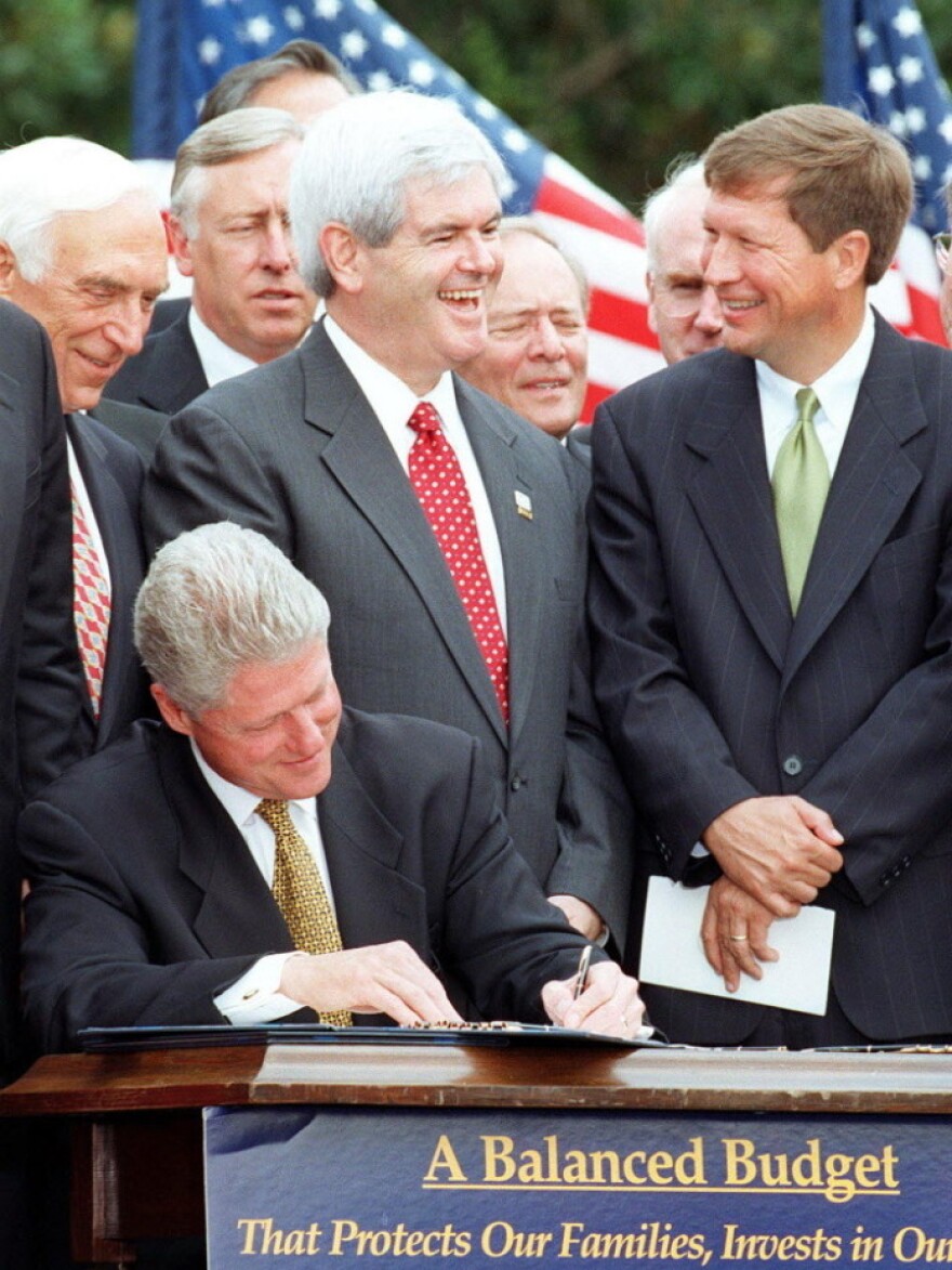 House Speaker Newt Gingrich talks with Rep. John Kasich of Ohio while President Bill Clinton signs the Balanced Budget Agreement on the South Lawn of the White House in 1997. 