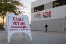 A man walks in front of a beige building near a sign indicating early voting is underway.