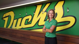 A woman stands in front of a wall. The word "ducks" is written on the wall. A wooden bench lines the wall. 