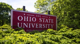 A red sign reading The Ohio State University stands in a bunch of bushes.