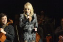 Dolly Parton stands on stage holding a microphone wearing a bedazzled outfit. 