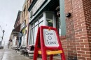A sign on a child-sized easel reads, "Open Today!" It sits on a sidewalk outside a row of shops in Newton Falls.