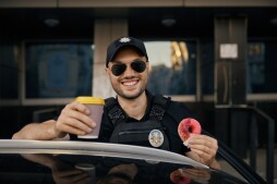 Portrait of happy patrolman drinking coffee eating donut traditional sweet while having lunch time at work. Professional city street order guardian and authority surveillance