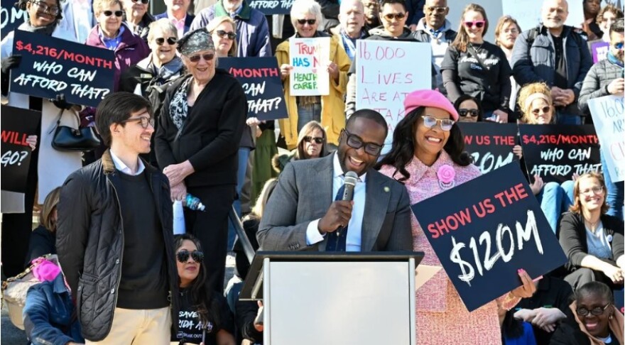 People carry signs that say "show us the 120 million" and "$4,216 a month, who can afford that?"