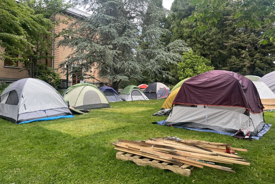 tents and wooden poles on a lawn surrounded by trees and a brick buidling.