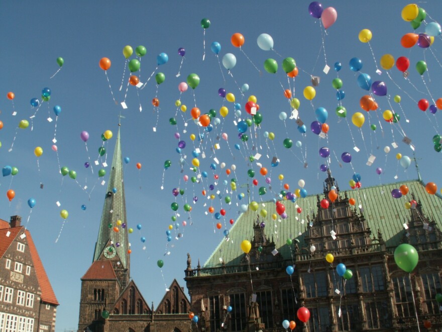Dozens of colorful balloons against a bright blue sky, above a medieval church. It's so beautiful and vibrant, it almost looks like clip art.