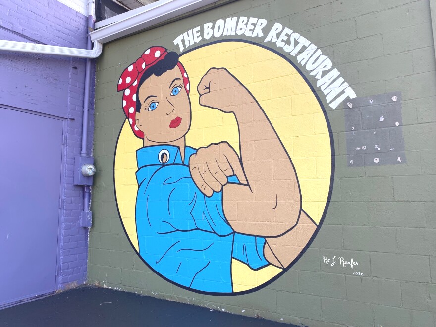  A large mural outside one of the walls of the Bomber that depicts Rosie the Riveter and reads "The Bomber Restaurant."