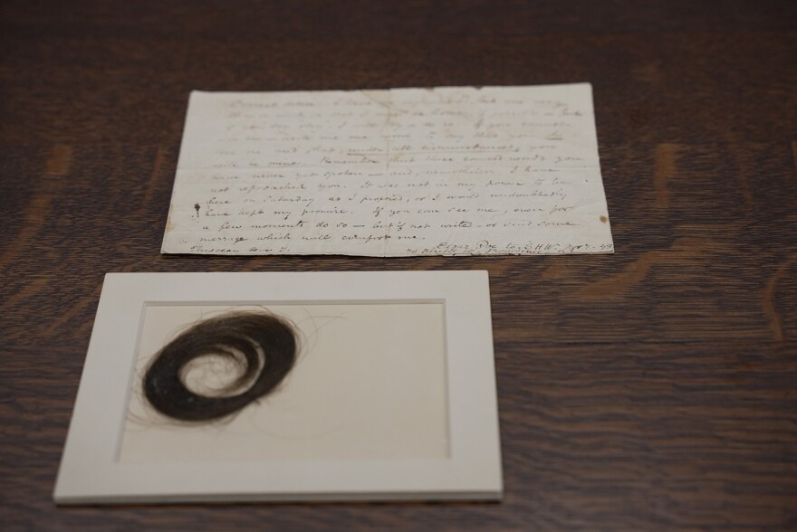 A lock of hair in a cardboard frame in the front; an old handwritten letter in the back, with the name Edgar Poe barely visible at the bottom