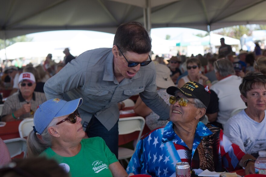 Retired Army Capt. Sam Brown leans over two people who are sitting. The people are looking up at Brown as he talks. 