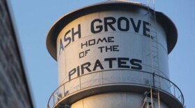 A water tower in the city of Ash Grove, displaying the name of the city and the name of the local school district's mascot.