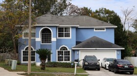 A light blue, two-story home with three cars parked in its driveway