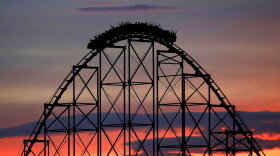 In this July 3, 2017, file photo, people ride a roller coaster at dusk at the Worlds of Fun amusement park in Kansas City. The park announced Wednesday that guests younger than 16 years old will be required to have a 21-year-old chaperone to gain entrance to the park.