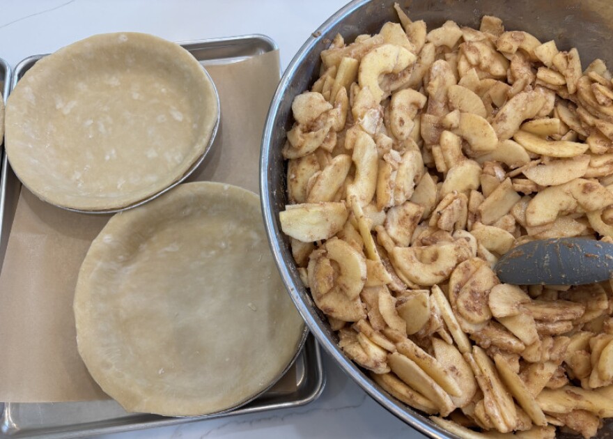 Empty pie shells next to a bowl of apple pie filling