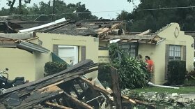 house damaged by tornado, with debris in front of house