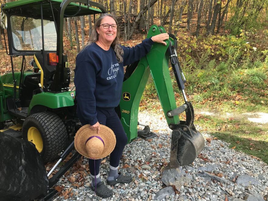 A woman holding a straw hat with her hand on a green tractor