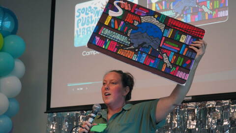 Kim McMilin holds aloft an enlarged prop version of one of three new limited edition library card designs unveiled Tuesday, Sept. 1, 2026 at the Soldotna Public Library in Soldotna, Alaska.