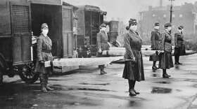 In this October 1918 photo made available by the Library of Congress, St. Louis Red Cross Motor Corps personnel wear masks as they hold stretchers next to ambulances in preparation for victims of the influenza epidemic. (Library of Congress via AP)
